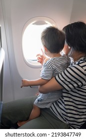 Infant traveling in airplane sitting on its mother lap both looking out of an airplane window. One year old baby boy flying in airplane and trying to entertain himself - Shutterstock ID 2193847749