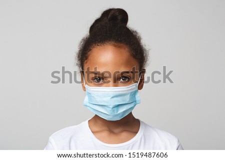 Infection concept. Portrait of little african american girl wearing medical mask, grey background