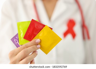 Infectious Disease Doctor With Red Ribbon On Uniform Holds Lot Of Condoms In Hand Closeup. Prevention Of Infection Of Sexually Transmitted Infections Concept.