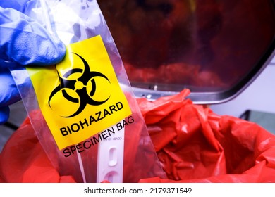 Infectious Garbage Of Covid-19 Test In Biohazard Specimen Bag Is Being Thrown Into The Red Infectious Waste Bin By The Doctor Hand