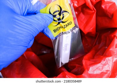 Infectious Garbage Of Covid-19 Test In Biohazard Specimen Bag Is Being Thrown Into The Red Infectious Waste Bin By The Doctor Hand