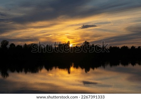 Infernal sunset behind trees and reflection in water.