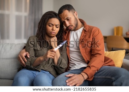 Infertility Problem. Depressed Black Couple Holding Negative Pregnancy Test Hugging Sitting On Couch At Home. Reproduction Health Problem, Childbirth Issues Concept