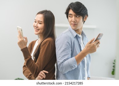 Infidelity, Suspicion Asian Young Couple Love Standing Back To Back, Husband Watching His Wife Using Mobile Phone, Spying His Girlfriend While Woman Typing A Message, Man Distrust And Jealousy At Home