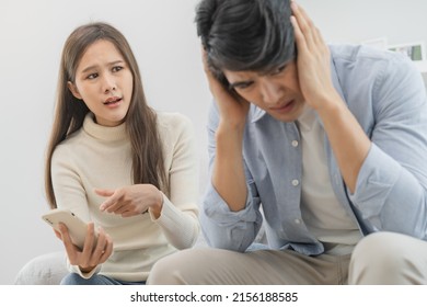 Infidelity, suspicion asian young couple love fight relationship, wife holding cellphone, smartphone cheating on phone, scolding husband about mistrust, distrust and jealousy when sitting at home. - Shutterstock ID 2156188585