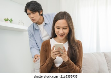 Infidelity, suspicion asian young couple love, wife using mobile phone, husband watching spying his girlfriend while woman chat a message, man sneaky distrust and jealousy, relationship problem. - Shutterstock ID 2165355935