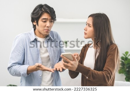 Infidelity, suspicion asian young couple love fight relationship, wife holding cellphone, smartphone cheating on phone, scolding husband about mistrust, distrust and jealousy at home.