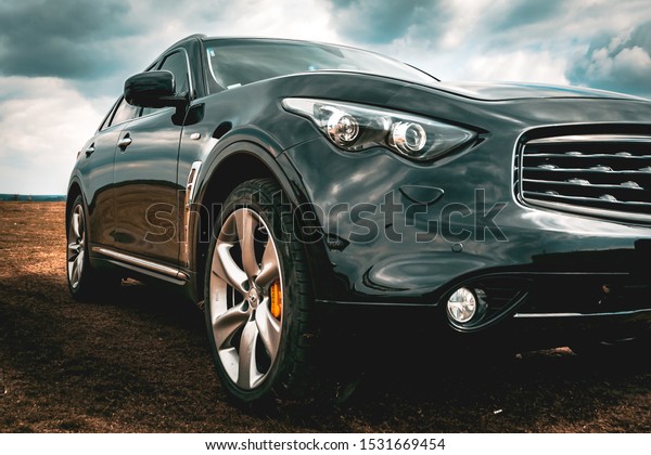 Infiniti QX70. Front side close up view of modern\
luxury black car xenon lamp headlight and LED fog lights. Beautiful\
cloudy sky reflection, carbon front grill, modern and prestigious\
SUV FX50