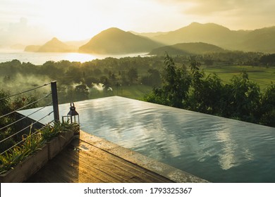 Infinity Pool With Amazing Mountain And Ocean View At Sunset. Sun Rays And Mist. Cloud Reflection In Water. Luxury Hotel Viewpoint.