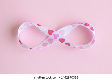 Infinity symbol made of heart design ribbon against pastel pink background minimal creative love concept.