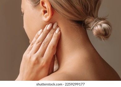 Inflamed tonsillar lymph nodes. Young woman touches enlarged lymph nodes under jaw on her neck with hand on dark background. Flu, cold, tonsillitis, sars virus, inflamed tonsils, bacterial infection