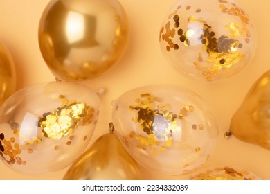 Inflatable balloons with confetti inside on a gold colored background. Festive creative concept. Selective focus.