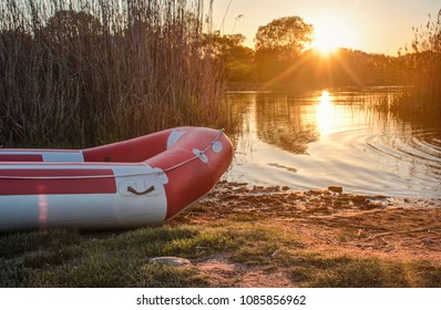 Inflatable Boat On The River Bank On Sunset Background