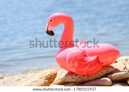 
Inflatable little pink flamingo by the sea on the pebbles. Recreation and vacation concept, children's game and fun. Summer relaxation on the beach. The sun is shining brightly, weather is great