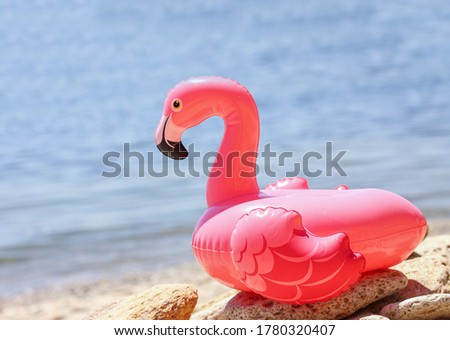Inflatable little pink flamingo by the sea on the pebbles. Recreation and vacation concept, children's game and fun. Summer relaxation on the beach. The sun is shining brightly, weather is great