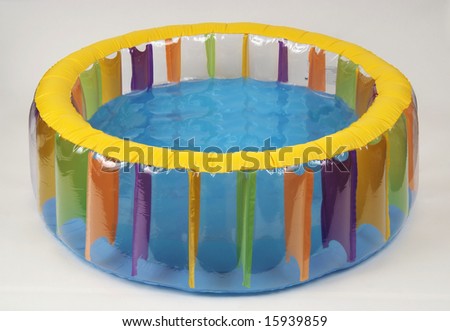 Inflated blue round paddling pool with sand and water on gray asphalt on a construction site with barrier in springtime sunshine in the city center of Wuppertal in North Rhine-Westphalia, Germany