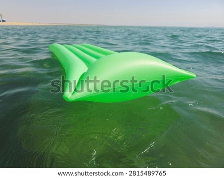An inflatable pool float lounge mattress drifting on water, classic ribbed vinyl water rafts, with integrated raised pillow headrest, for sunbathing, lounging, and drifting on pool, lake, or beach waters