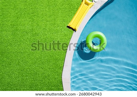 Inflatable ring floating in swimming pool surrounded by green grass, top view
