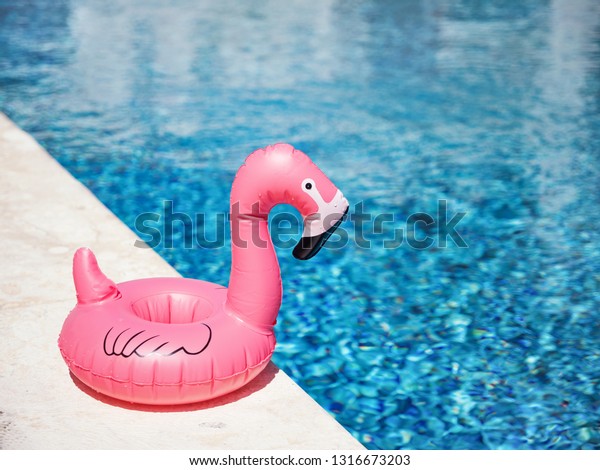 Inflatable toy of pink flamingo near swimming pool\
at poolside, nobody