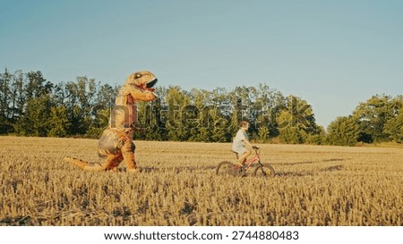 Inflatable T-Rex Chasing Boy Riding Bicycle in Sunny Open Field. Childhood fun. High quality photo