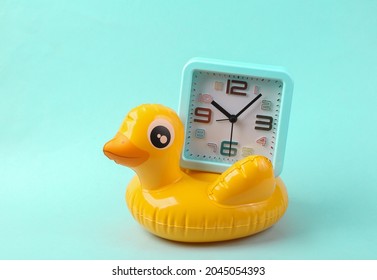 Inflatable yellow duck with alarm clock on blue background. Summer time concept