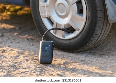 Inflating car tires with a portable wireless air pump outdoor. - Shutterstock ID 2313196601