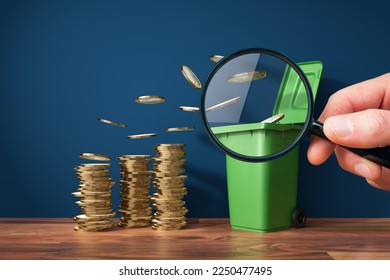 Inflation concept - coins fly to garbage can. Visual metaphor of devaluation of savings by inflation. Magnifying glass in hand focus on part of coins and dustbin container. - Shutterstock ID 2250477495