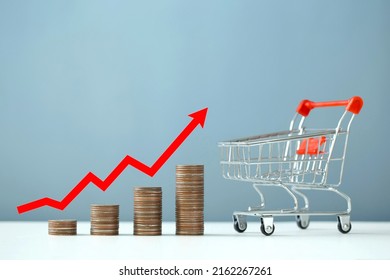 Inflation and the economic crisis. Financial market crash. The red arrow on the chart is pointing up at the stacks of coins and shopping cart. higher inflation rate compared to the product received. - Powered by Shutterstock