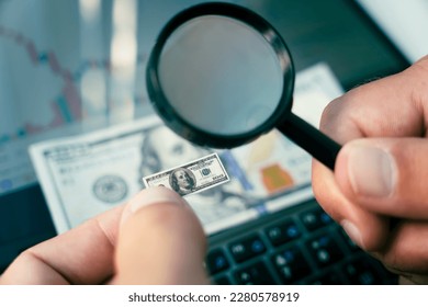 Inflation shrinking value of US dollar. a trader looks at a small dollar in his hand through a magnifying glass