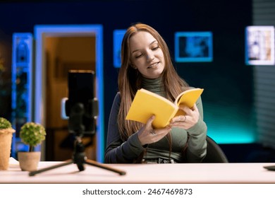 Influencer in studio using camera to capture live broadcast, reviewing new book from publisher. Online show host filming literature critique, presenting new novel from esteemed author to viewers