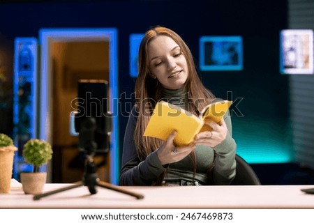 Influencer in studio using camera to capture live broadcast, reviewing new book from publisher. Online show host filming literature critique, presenting new novel from esteemed author to viewers