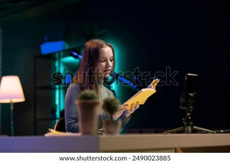 Influencer in studio using camera to capture footage, reviewing hardcover book from publisher. Young reading hobbyist filming literature critique, presenting new novel from author to readers