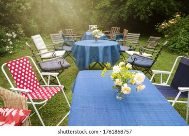 Informal Garden Party Set Up With Tables, Blue Tablecloths And Different Chairs In A Countryside Backyard, Selected Focus