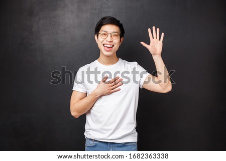 Informal greeting concept. Outgoing attractive young asian guy introduce himself in front of team, raise hand and pointing at him as saying own name, smiling hello gesture, black background