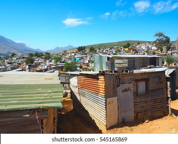 Informal Settlements, Huts Made Of Metal Or Zinc In The Township Or Cape Flats Of Stellenbosch, Cape Town, South Africa With Mountain And Blue Sky And Clouds Background, Slum