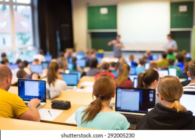 Informatics Workshop At University. Rear View Of Students Sitting And Listening In Lecture Hall Doing Practical Tasks On Their Laptops.