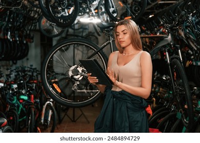 Information in the digital tablet, standing. Repair woman in bicycle shop, working in store. - Powered by Shutterstock