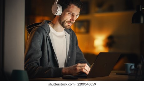 Information Technology Specialist Working Late On Latptop. Software Engineer Wearing Hoodie, Typing On Computer In His Cozy Home Office Apartment. Remote Work Concept. View From Outdoors Into Window.