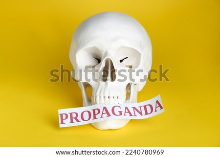 Information warfare concept. Human skull and paper card with word Propaganda on yellow background