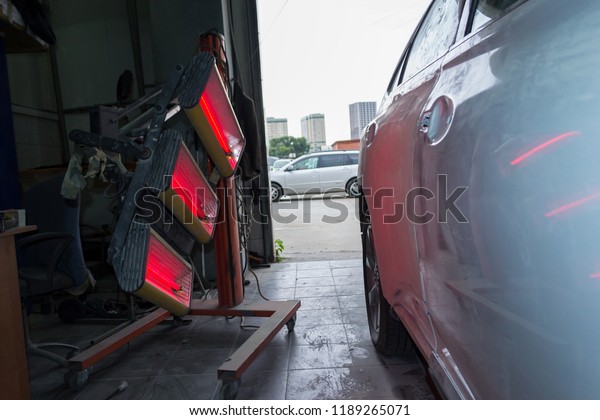 Infrared drying of white car body parts after\
applying putty and paint on a white suv vehicle in the body repair\
shop with red lanterns in the working environment using a special\
tool and equipment