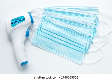 Infrared Electronic Thermometer Gun And Medical Surgical Mask For Protection Face From Pollution. A Device For Measuring Human Temperature. Covid-19 Prevention Concept.