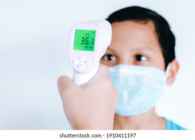 Infrared thermometer in a hand measuring the temperature of the asian little boy with  protective surgical mask on the face