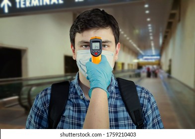 An Infrared Thermometer Is Pointed To A Young Man's Forehead In A White Medical Mask. Airport Staff Checks The Temperature Of Passengers.