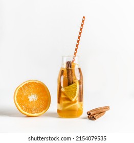 Infused Water Bottle With Drinking Straw And Ingredients: Orange And Cinnamon Sticks At White Background. Summer Refreshing Drink With Fresh Fruits. Healthy Lifestyle. Front View.