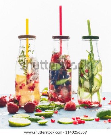 Infused water in bottles with drink straw and ingredients on white background, front view. Water Flavored with fruits, berries and herbs. Summer drinks. Healthy and clean detox beverages.