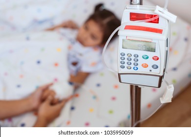 Infusion Pump Feeding IV Drip Into Child Patient While Mother Holding Daughter Hand With Love And Care In The Hospital