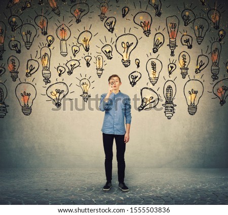 Ingenious teenage boy seeking for brilliant ideas as looks curious through the magnifying glass. Student boy try to find solutions to every problem as lots of light bulbs surrounds him.