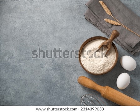 Ingredients for baking, wheat flour, eggs, rolling pin and kitchen textiles on a blue background. Homemade healthy food concept. Top view and copy space.