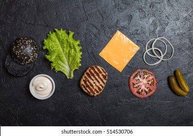 Ingredients For Cooking Black Burger. Grilled Chicken Patty, Buns, Onion, Tomatoes, Lettuce, Pickles, Sauce, Cheese Over Black Background Top View