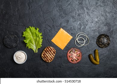 Ingredients For Cooking Black Burger. Grilled Chicken Patty, Buns, Onion, Tomatoes, Lettuce, Pickles, Sauce, Cheese Over Black Background, Top View